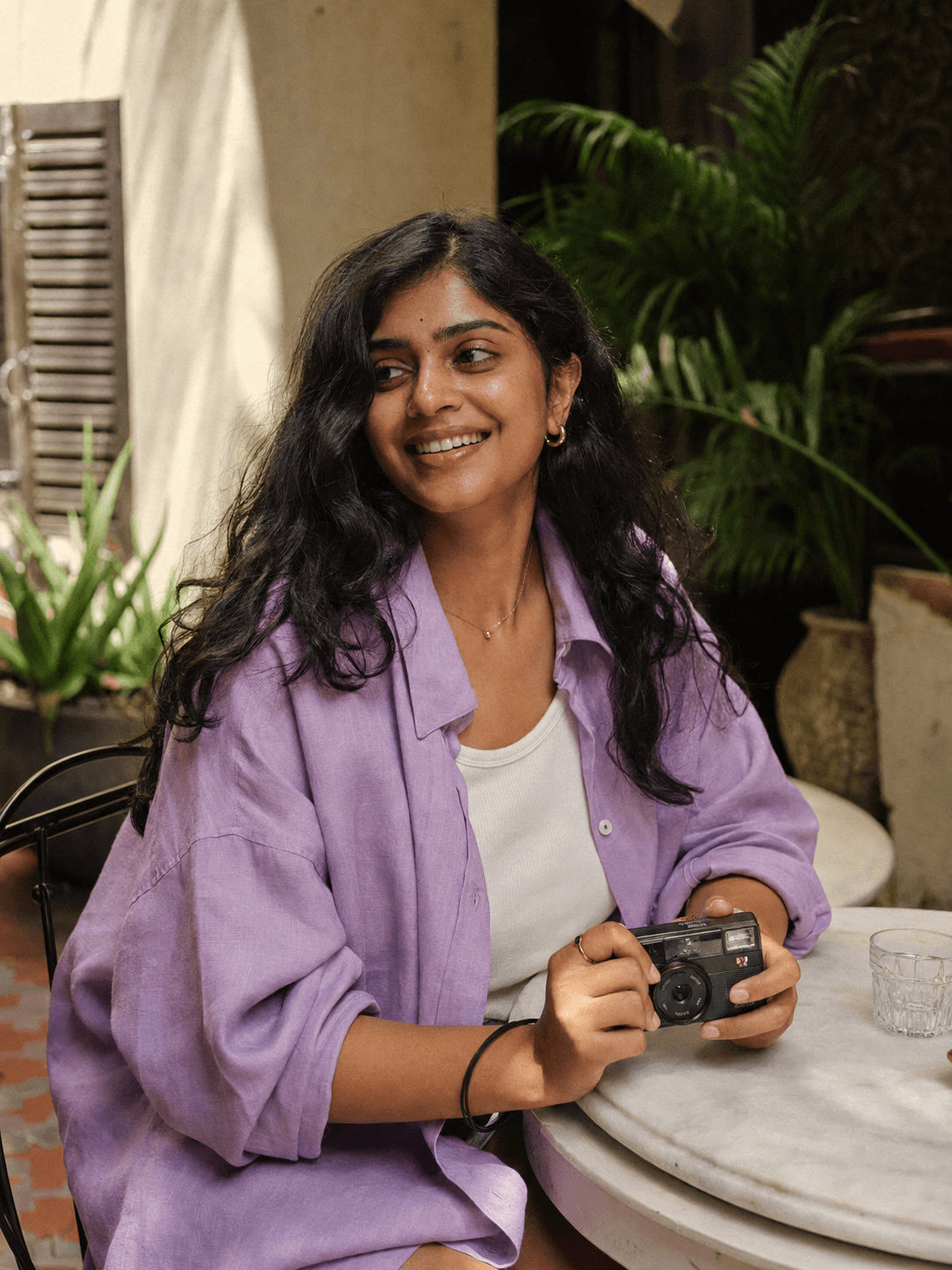 Portrait of Meera, a fictional lifestyle creator, holding a camera in a courtyard